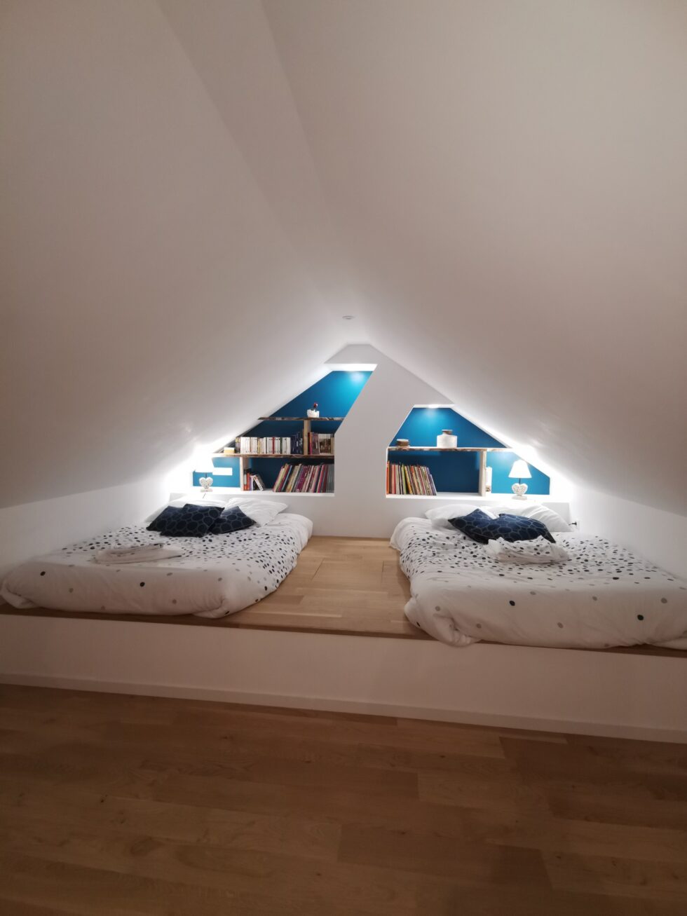 combles aménagés en chambre avec deux lits et des espaces de rangement intégrés
